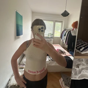 Vit croppad Juicy Couture linnetopp - Säljer en vit croppad linnetopp från Juicy Couture med rosa logga längs nederkanten. Toppen har halterneck och är ärmlös, perfekt för en trendig och avslappnad look. Materialet är stretchigt och mjukt, vilket gör den superbekväm.