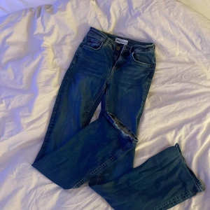 Blå bootcut jeans från Zara, stl 34 - Säljer ett par blå jeans från Zara i storlek 34. Jeansen har klassisk femficksdesign, normalhög midja och bootcut-ben som ger en snygg siluett. Tillverkade i mjukt denimtyg med lätt tvättad look. Perfekta för dig som gillar en tidlös och trendig stil.