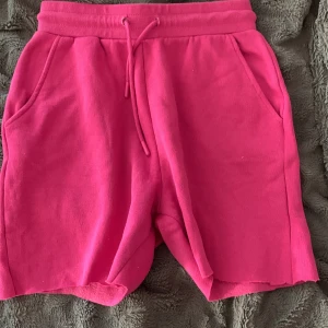 Rosa mjuka shorts från FB Sister - Säljer ett par knallrosa mjukisshorts från FB Sister i storlek XS. De har resår i midjan med snörning och två sidofickor. Perfekta för chill dagar eller när du vill vara bekväm men ändå se färgglad ut.