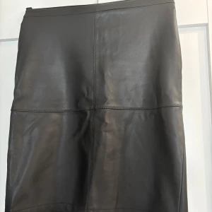 Svart skinnkjol (fakeskinn) XS - Snygg svart skinnkjol (fakeskinn) med markerade sömmar och en liten stilren slits baktill. Kjolen har en rak passform. Passar till både boots och sneakers. Storlek XS. Köpare står för frakten. 