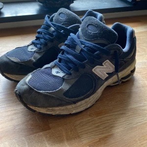 New Balance 2002R  - Säljer ett par New Balance 2002R sneakers i mörkblått med vita detaljer. Skorna har mesh och mocka i ovandelen, klassisk N-logga på sidan och snörning framtill. Sulan är vit med svarta partier och ger en sportig vibe. Perfekta för dig som gillar retrostil och streetwear.