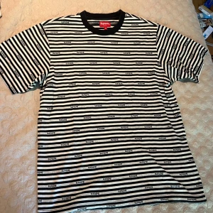 Randig Supreme t-shirt svart/vit - Supreme t-shirt i svart och vitt med horisontella ränder och loggan tryckt i varje rand. Klassisk crewneck med svart krage och korta ärmar. Skön och avslappnad passform, perfekt för dig som gillar streetwear och vill sticka ut.
