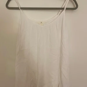 Vit linnetopp från H&M L.O.G.G. - Säljer en vit linnetopp från H&M L.O.G.G. med smala justerbara axelband. Den är lätt v ringad och superfin till en kofta eller ett par jeans. Använt fåtal gånger och är iprincip nyskick.