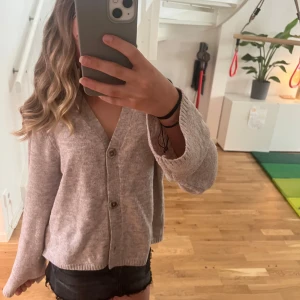 Beige stickad kofta med knappar - Mysig beige stickad kofta med v-ringning. Koftan har långa ärmar och en avslappnad passform, perfekt att slänga på sig när det är lite kyligare. Enkel och stilren design som funkar till det mesta. Jätte bra och värmade inför hösten, säljer pga den ej kmr till användning. Pris kan diskuteras