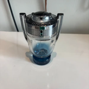 Paco Rabanne Invictus parfym (tom flaska) - Säljer en Paco Rabanne Invictus parfym i den ikoniska troféformade flaskan. Flaskan är genomskinlig med blå botten och har ett silvrigt lock med handtag på sidorna. Märket och namnet är ingraverat i metallen. Perfekt för dig som gillar fräscha och sportiga dofter.