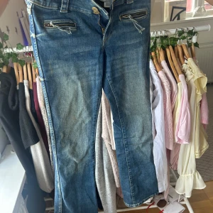 Blå jeans med dragkedjedetaljer - Snygga blå jeans med coola dragkedjor framtill. Jeansen har klassisk femficksdesign, slitningar och en något tvättad look. Perfekta för dig som gillar en avslappnad men ändå trendig stil.