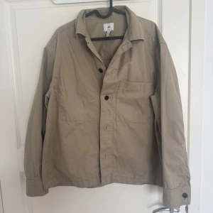 Beige HM overshirt  - Säljer en beige overshirt från H&M i loose fit. Jackan har klassisk krage, knäppning framtill med svarta knappar och stora fickor. Perfekt att slänga över en hoodie eller t-shirt för en chill look.