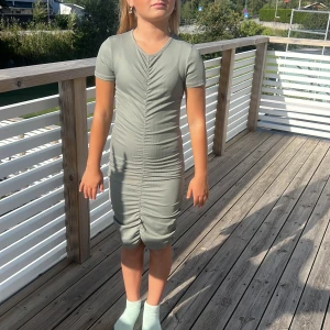 Grå ribbad klänning med rynk - Supersnygg grå ribbad klänning med korta ärmar och rynk längs hela mitten fram och bak. Klänningen är figurnära och har en cool, tight passform som framhäver siluetten. Perfekt för dig som gillar stilrena och trendiga plagg.