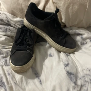 Svarta sneakers från Selected Homme - Svarta sneakers från Selected Homme med klassisk design och vita sulor. Skorna har snörning och är tillverkade i mocka med rund tå. Perfekta för en stilren och avslappnad look. Pris går att diskutera