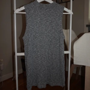 Grå ribbad ärmlös topp från Monki - Säljer en grå ärmlös topp från Monki i storlek XS. Toppen är ribbstickad och har en högre halsringning. Slit på sidorna. Perfekt att styla med jeans eller kjol för en chill och trendig look.