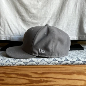 Grå LA-keps från New Era - Snygg grå keps från New Era med klassisk LA-logga broderad i vitt framtill. Kepsen har böjd skärm, broderade ventilationshål och MLB-logga baktill. Tillverkad i bomull för en bekväm passform och stilren look. Kepsen passar den som har lite större huvud!