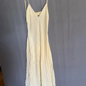 Ljusgul långklänning med öppen rygg - Långklänning i ljusgul nyans med smala axelband och v-ringning. Klänningen har en snygg öppen rygg och är tillverkad i ett tunt, lätt material som ger ett flowy intryck. 