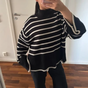 Svartvit randig stickad polotröja - Oversized svart stickad polotröja med vita horisontella ränder. Tröjan har vida, långa ärmar och hög krage. Avslut och ärmslut har vit kant. Perfekt för dig som gillar en chill och trendig look.