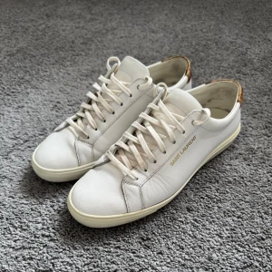Vita sneakers från Saint Laurent - Snygga vita sneakers från saint laurent. Skorna har snörning och är tillverkade i skinn, vilket ger en lyxig känsla. Perfekta för en stilren look. Dom är storlek 41 1/2 men sitter som 42.‼️ 