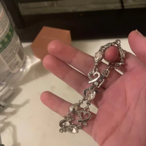 Silverfärgat armband med hjärtan - Superfint armband i silverfärg med flera berlocker i form av hjärtan och gnistrande stenar. Armbandet har detaljer som siffror och glittriga inslag, perfekt för dig som gillar bling och söta detaljer.