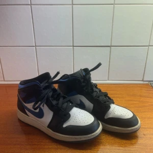 Nike Air Jordan 1 Mid svart/blå/vit - Säljer ett par Nike Air Jordan 1 Mid i svart, blått och vit. Jag säljer dom för dom har blivit för stora för mig, dom är lite smutsiga för dom har varit i min garderob i ungefär 1 år men jag kan tvätta dom innan jag postar dom så ser dom nästan nya ut, dom är lite creasade men inget man tänker på😊