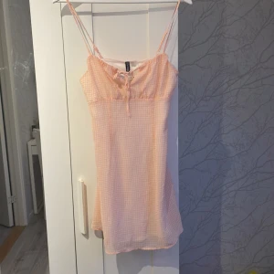 Rutig ljusrosa kortklänning H&M - Supersöt kortklänning från H&M i ljusrosa och vit rutig design. Klänningen har smala justerbara axelband, snörning framtill och dragkedja i sidan. Klänningen är helt oanvänd med prislapp kvar