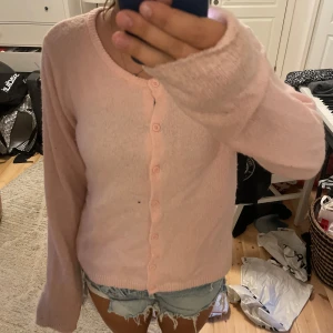 Ljusrosa kofta med knappar - Supermjuk ljusrosa kofta från 157 med rund halsringning och knäppning framtill. Långärmad och stickad i ett fluffigt material som känns riktigt cozy. Perfekt att slänga över en topp eller klänning för en söt look. Är ett litet hål j armhålan sån var där när jag köpte verkligen ingenting som märks🩷