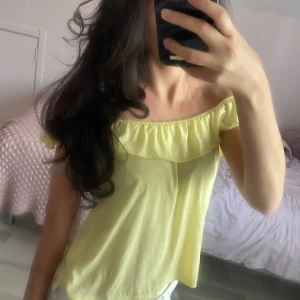 Gul offshoulder topp med volang - Söt ljusgul offshoulder topp med volang runt hela överdelen. Tunn och luftig, perfekt för varma dagar. Toppen har en lös passform och är ärmlös, vilket ger en avslappnad och trendig vibe.