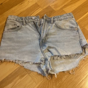 Ljusblå jeansshorts från 157 - Säljer ett par ljusblå jeansshorts från 157 med råa, fransiga kanter och klassisk femficksdesign. Shortsen har normal passform och är perfekta för varma dagar. De är tillverkade i denim och har en avslappnad vibe.