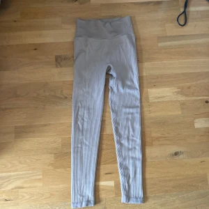 Beige ribbade leggings från Stronger - Säljer ett par snygga beige ribbade leggings från Stronger. De är högmidjade och har en tight passform som sitter skönt. Perfekta för träning. Materialet är stretchigt.