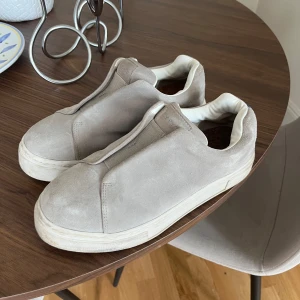 Grå sneakers från Eytys - Stilrena slip-on sneakers från Eytys i grått med vit sula och diskret lila detalj baktill. Skorna har en minimalistisk design utan snörning och en rund tå. Perfekta för dig som gillar en clean och modern look. Normala i storlek och nypris är på 2200kr!🖤🪩