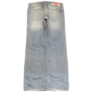  True Religion jeans - jeans från True Religion i ljusblå denim med klassiska kontrastsömmar och stora bakfickor med broderad logga. Snygg vintagekänsla och avslappnad passform, perfekt för dig som gillar streetstyle och denim. storlek 36x34, ben öppning 22 cm! använd gärna köp nu 😇