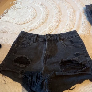 Svarta jeansshorts från Jennyfer - Snygga svarta jeansshorts från Jennyfer med hög midja och slitna detaljer framtill och nertill