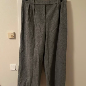 Grå kostymbyxor med resår - Snygga grå kostymbyxor med rak passform och resår i midjan baktill för extra komfort. Byxorna har klassisk look med pressveck och bälteshällor framtill. Perfekta för en clean och stilren outfit.Katt finns i hemmet 