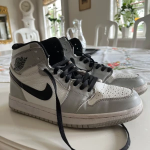 Nike Air Jordan 1 High vit/grå - Snygga Nike Air Jordan 1 High sneakers i vitt och ljusgrått skinn med svarta detaljer. Säljer dom billigt då jag vill bli av med dom. Har inte kvar lådan. Storlek 41. Bra skick
