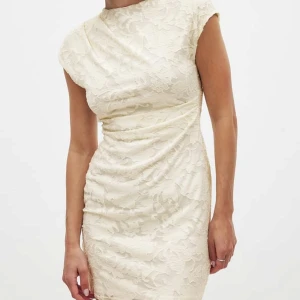 Vit spetsklänning med öppen rygg - Superfin vit kortklänning med blommig spets och öppen rygg. Klänningen har korta ärmar, figurnära passform och snygga draperingar i midjan. Helt oanvänd med prislapp kvar!