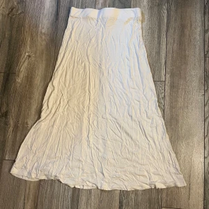 Vit långkjol i bomull - Enkel och flowy vit långkjol i mjukt bomullstyg. Kjolen har en rak och avslappnad passform som ger en chill vibe, perfekt för varma dagar. Stilren och lätt att matcha med olika toppar och accessoarer.