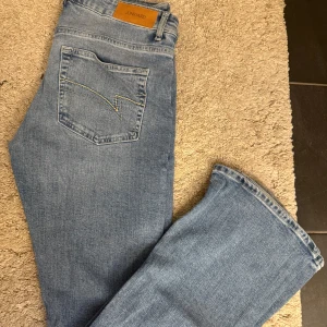 Ljusblå bootcut jeans från Junkyard - Snygga ljusblå jeans från Junkyard med klassisk femficksdesign och bootcut-ben. Jeansen har en cool bakficka med kontrastsöm och är tillverkade i mjukt bomullsjeans. Perfekta för dig som gillar retrovibbar och avslappnad stil.