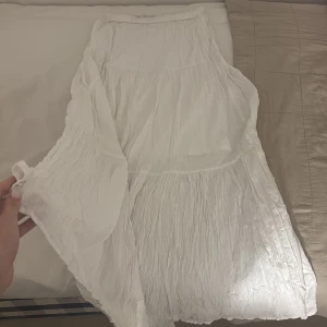 Vit långkjol i bomull med volang - Superfin vit långkjol i luftig bomull med flera volanger och lätt skrynklig struktur. Perfekt för varma dagar och ger en chill och bohemisk vibe. Resår i midjan för skön passform.