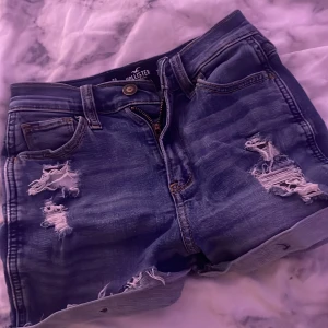 Blå slitna jeansshorts Hollister - Snygga blå jeansshorts från Hollister med hål.  Modellen är midwaist och har en avslappnad passform. Passar en XS och S!