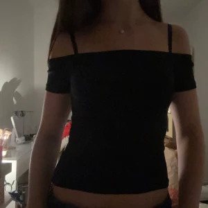 Svart offshoulder topp - Snygg svart offshoulder topp med smala axelband och korta ärmar. Tight passform som framhäver figuren och passar perfekt till jeans eller kjol. Enkel och stilren design som är lätt att matcha med olika accessoarer.
