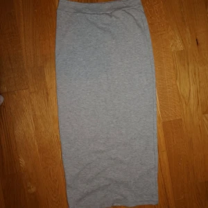 Grå långkjol i bomull - Enkel och stilren grå långkjol i mjukt bomullsmaterial. Kjolen har rak passform och är perfekt för dig som gillar en clean och avslappnad look. Lätt att matcha med både sneakers och boots.