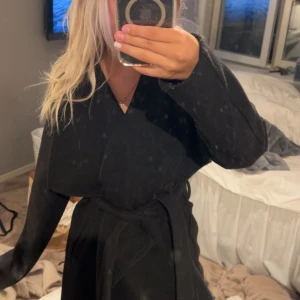 Svart omlottkappa med bälte - Säljer en svart kappa med omlottmodell och bälte i midjan.  Den är märket vila köpt på zalando nypris kanske 699 den är lite för stor för mig