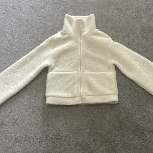 Vit teddyjacka i XS med dragkedja - Mysig vit teddyjacka i storlek XS med hel dragkedja framtill och två stora fickor. Jackan har hög krage och är tillverkad i fluffigt teddy-material som ger en chill och trendig look. Perfekt för lager-på-lager och passar till allt. Jackan är i väldigt bra skick. Säljer p.g.a för liten storlek för mig i längden (jag är 160 cm lång). Skriv för fler bilder.
