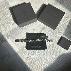Emporio Armani silverfärgat armband - Stilrent armband från Emporio Armani i silverfärgat rostfritt stål med breda länkar och den klassiska Armani-loggan ingraverad på plattan. Kommer med originalask och svart förvaringspåse. Perfekt accessoar för en clean och modern look.