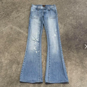 Blå bootcut jeans från Hollister - Sjuktnsugga ljusblå bootcut jeans från hollister med slitningar, färgstänk och coola detaljer på bakfickorna. Klassisk femficksmodell i bomull med dragkedja och knapp framtill. Perfekta för dig som gillar en avslappnad och trendig look. Kolla bilder för mått! Köpte dessa från en amerikansk användare på depop för  ungefär 1200kr och de är som nya! Passade dock inte mig :/ xs/s eftersom jag är osäker på ifall jag vill sälja så tar jag inte prissänkningar! Det är 700kr som gäller!