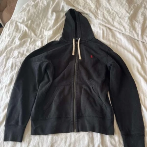 Svart zip hoodie från Polo Ralph Lauren - Svart zip hoodie från Polo Ralph Lauren med dragkedja, vit snörning i huvan och röd broderad logga på bröstet. Storlek M
