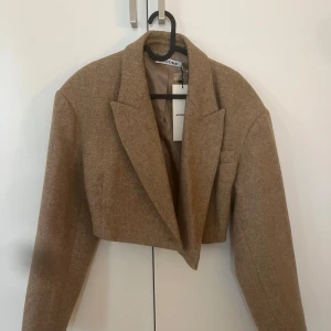 Beige croppad kavaj från Adoore - Snygg croppad kavaj från Adoore i beige ullmix. Klassisk krage, långärmad och med stilren passform.