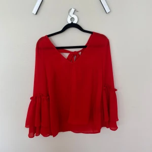 Röd blus med volangärm från H&M  - Röd blus från H&M med v-ringning och knytning i ryggen. Vida volangärmar med söt rynkdetalj vid armbågen. 