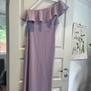 Ljuslila långklänning från Lulus oneshoulder - Superfin ljuslila långklänning från Lulus med oneshoulder och volangdetalj över bysten. Klänningen har en slimmad passform och är tillverkad i ett mjukt, stretchigt material som sitter snyggt. Perfekt för bal eller avslutnings middag! Köpte för 1050kr och säljer nu för 600kr men kan sänka vid snabb affär. Endast använd en gång.❤️