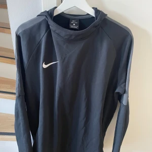 Svart långärmad tröja från Nike - Säljer en svart långärmad tröja från Nike med Dri-FIT-teknologi. Perfekt för träning med sin bekväma passform och stilrena design. Den har en liten Nike-logga på bröstet. Passar bra för aktiva dagar.