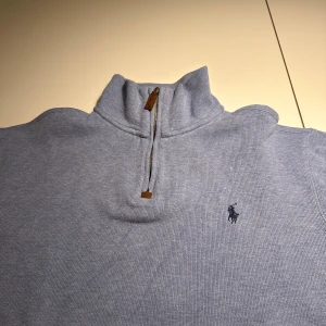 Ljusblå tröja från Polo Ralph Lauren - Säljer en stilren ljusblå tröja från Polo Ralph Lauren med dragkedja vid halsen. Tröjan har en broderad logotyp på bröstet och är perfekt för en avslappnad look. Passar bra till både jeans och chinos.