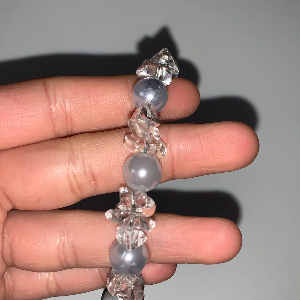 Elegant armband med skimrande grå pärlor och klara kristaller. Armbandet har en justerbar kedja med en guldfärgad detalj vid låset. Perfekt för att ge en glittrig touch till din stil.. Asusteet.