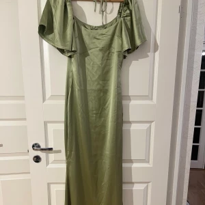 Grön långklänning i satin - Säljer en helt oanvänd elegant grön långklänning i satin. Klänningen har en vacker glans och faller fint längs kroppen. Perfekt för festliga tillfällen! Storlek 38 men passar även 36.