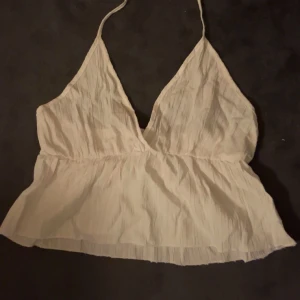 Vit ärmlös linnetopp - Säljer en söt vit ärmlös linnetopp med smala axelband som man knyter runt halsen och v-ringning. Toppen har en luftig och lätt design, perfekt för varma dagar. Den är enkel och stilren, vilket gör den lätt att matcha med olika outfits💕.